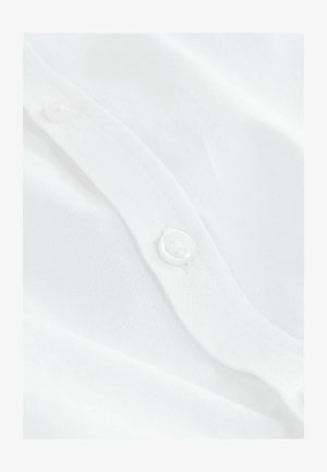 Prim-plan al unei țesături albe cu o textură netedă, având un buton alb mic și rotund aproape de margine și un model fin, subtil.