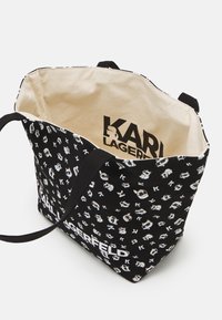 Musta kangaskassi, jossa valkoisia sarjakuvamaisia kuvioita ja "KARL LAGERFELD" -logo. Sisältä vaaleanbeige kangas, jossa painettu brändäys. Kaksi mustaa hihnaa.