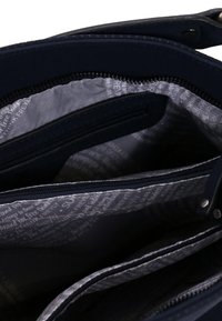 Dunkelblaues Handtascheninnere mit mehreren Reißverschluss- und offenen Fächern, die mit einem hellgrauen Stofffutter mit bedrucktem Text versehen sind.