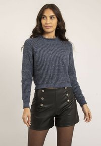 Pull en maille bleu marine avec un motif texturé et des manches longues, associé à un short en cuir noir taille haute avec des boutons métalliques.
