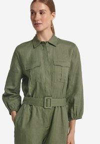 Grön linneklänning med krage, två bröstfickor, elastiska ärmar och ett bälte i midjan. Erbjuder en avslappnad passform och en mjuk textur.