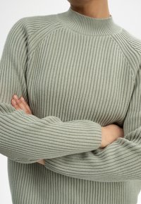 Hellgrüner gerippter Pullover mit hohem Kragen und langen Ärmeln, der ein strukturiertes Strickmuster und eine lockere Passform aufweist.