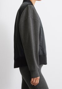 Zwart-grijs bomberjack met een gladde, glanzende voorkant, zachte getextureerde mouwen, geribbelde manchetten en een aangesloten tailleband. Zijkantzakdetail zichtbaar.