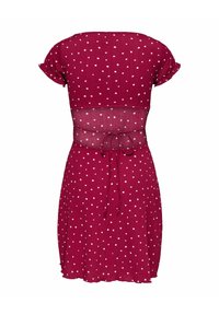 Robe rouge à manches courtes avec des pois blancs, panneau transparent au milieu du dos et détail à nouer à la taille, vue de dos.
