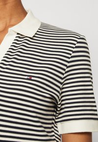 Gestreiftes Polo-Shirt aus Baumwolle in Schwarz und Weiß mit einem kontrastierenden weißen Kragen. Verfügt über kurze Ärmel und ein kleines Logo auf der Brust.