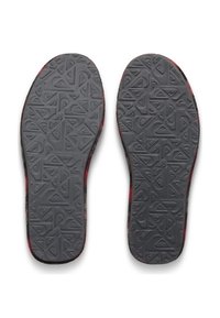 Schuhsohlen mit grauen, geometrischen Profilmustern, die leichte Abnutzung an den roten und schwarzen Kanten vor weißem Hintergrund zeigen.