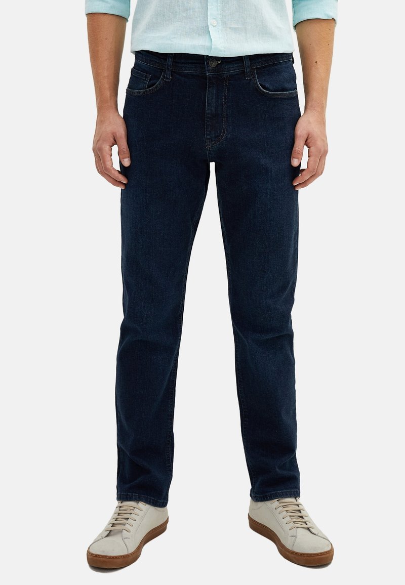 Dark blue denim jeans with a classic straight-leg cut, five-pocket design, and subtle stitching details, paired with light-colored sneakers.