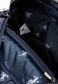 Námorní interiér tašky s hladkou texturou, který obsahuje opakující se bílý vzor loga a stříbrný zip s táhlem na logo.