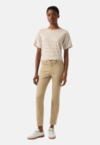 Gestreept T-shirt met korte mouwen in beige en crème, gecombineerd met aansluitende kaki broek en witte sneakers. Soepele katoenen textuur, casual design.