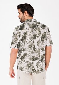 Camisa de manga corta en tejido ligero con estampado de hojas verdes. Presenta un cuello, cierre frontal con botones y un dobladillo recto.