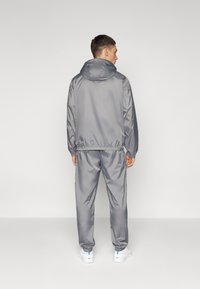 Grey tracksuit made of smooth, lightweight material with an elastic waistband and cuffs, featuring a hood and minimal stitching details.