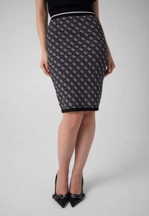 Donna in piedi che indossa una gonna a tubino a fantasia bianca e nera al ginocchio con tacchi alti neri con dettagli di fibbie.