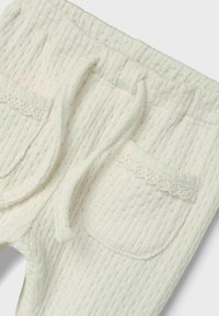 Crèmekleurige gebreide broek met een gestructureerd ribbelpatroon, elastische tailleband, trekkoord en kantafwerking op de zakken.