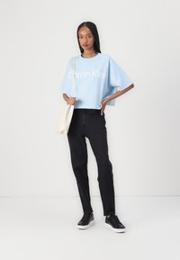 Ljusblå kortärmad t-shirt med vit "Calvin Klein"-logotyp, kombinerad med svarta högmidjade jeans och svarta sneakers. Enkel axelväska.