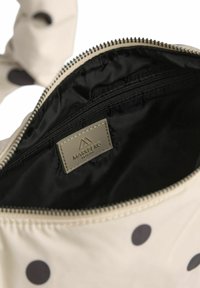 Beige taske med sorte prikker, med sort foer, lynlåslukning og et mærketag indeni.