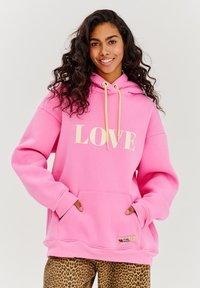 Růžová mikina s kapucí a potiskem "LOVE" v krémové barvě, se šňůrkami a přední kapsou, v kombinaci s kalhotami s leopardím potiskem.