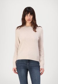 Jasno beżowy sweter wykonany z miękkiego materiału, z okrągłym dekoltem i ściągaczami na rękawach. W zestawie z ciemnoniebieskimi dżinsami dla kontrastu.