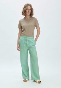 Hellbraunes T-Shirt mit kurzen Ärmeln, kombiniert mit lockeren, mintgrünen Hosen mit Kordelzug. Das Model trägt beiges Sandalen; glatte Stofftextur.