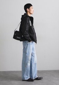 Giacca leggera nera con cappuccio, abbinata a jeans in denim azzurro chiaro a gamba larga con cuciture a contrasto e scarpe in pelle nere.