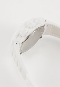 Montre blanche avec un bracelet en caoutchouc texturé, quincaillerie argentée et un boîtier métallique rond. Comprend trois boutons sur le côté, arrière lisse.