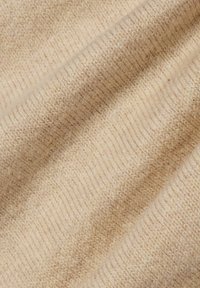 Beiges Strickgewebe mit weicher Textur, das ein geripptes Muster und subtile Farbvariationen im gesamten Material aufweist.