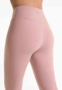 Lichtroze high-waisted leggings gemaakt van een gladde, rekbare stof. Kenmerken een matte afwerking met minimale branding op de tailleband.