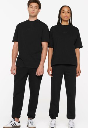 Black cotton unisex outfit featuring short-sleeve shirts and matching tapered joggers. Subtle branding in the center of the shirts.