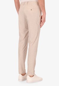 Pantaloni leggeri beige con finitura testurizzata, slim fit, dotati di tasche posteriori e dettagli cuciti, abbinati a sneaker bianche.