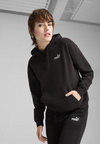 Felpa nera con cappuccio e tasca a marsupio, con il logo grigio Puma sul petto, abbinata a pantaloni della tuta neri con il logo Puma.
