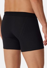 Boxer briefs neri a coste con una vestibilità aderente, caratterizzati da un elastico morbido e sottili righe dorate lungo la trama del tessuto.