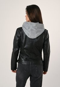 Zwarte leren jas met een grijze sweatshirtcapuchon, slim-fit ontwerp, gestructureerde afwerking en zichtbare stikdetails. Zwarte denim broek.
