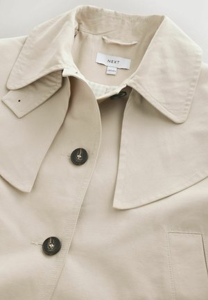 Beiger Trenchcoat mit großem Kragen, dunklen Knöpfen, Schulterklappe und Markenetikett "NEXT" im Krageninnenteil.
