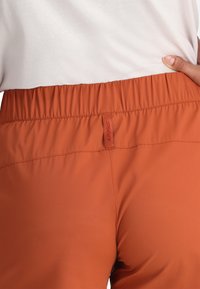Oranje sportbroek met een rekbare, soepele textuur en een elastische tailleband. Het merkembleem is zichtbaar op de achterkant.