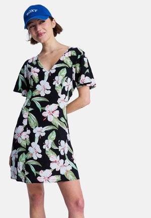 Zwarte jurk met een bloemenpatroon met witte bloemen en groene bladeren. V-hals ontwerp en korte, wijd uitlopende mouwen. Katoenen textuur.