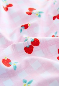 Tessuto di cotone con un motivo a scacchi rosa, decorato con fragole rosse e foglie verdi. Texture liscia con dettagli floreali colorati.