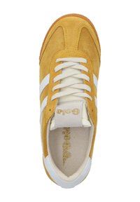 Gula mockaskor med vita ränder, vita snören och en beige innersula. Har en guldfärgad logotyp på tungan. Platt gummisula.