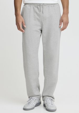 Pantalon de survêtement gris en tissu doux, doté d'une taille élastique et d'une coupe décontractée. Associé à des chaussures de sport grises.
