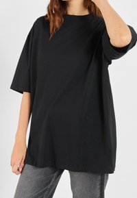 Czarna bawełniana koszulka z luźnym krojem, okrągłym dekoltem i krótkimi, szerokimi rękawami, w zestawie z szarymi dżinsami. Minimalistyczny design bez wzorów.