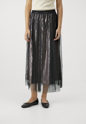 Gonna di tulle nera con finitura metallizzata, caratterizzata da una ampia vita elastica, design fluido e texture a strati. Indossata con ballerine nere.