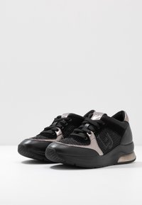 Scarpe sportive nere realizzate in materiali mesh e pelle, dalla forma arrotondata, con dettagli testurizzati e un elemento metallico sul lato.