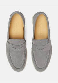 Mocassini in suede grigi con profilo basso, cuciture decorative sulla parte anteriore e una suola liscia di colore chiaro. Nessun elemento di metallo o dettagli visibili.