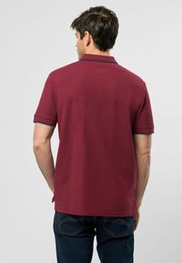 Bordó polo tričko s krátkými rukávy, ribovaná textura a tmavě modré akcenty na manžetách. Má rovný lem a decentní design límečku.