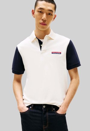 Polo à manches courtes en crème et marine, avec un col classique, le logo brodé « HILFIGER » et une coupe décontractée. Porté avec un jean foncé.