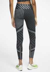 Czarne legginsy z geometrycznymi wzorami, w tym chevronami i kratkami, z wysokim stanem i zamkami przy kostkach. Wykonane z elastycznego materiału.