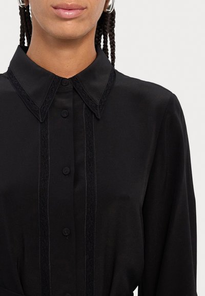 Blusa negra con cuello de tipo camisa, con un delicado encaje en la parte delantera y los puños, tejido suave y silueta ajustada.