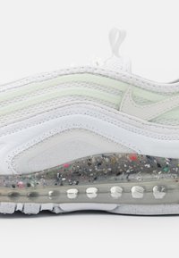 Bílé tenisky vyrobené z vrstvené síťoviny a syntetických materiálů, s průhlednou vzduchovou podrážkou s mnohobarevnými skvrnami a světle zeleným akcentem.