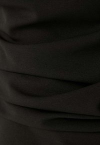 Zwarte stof met een zachte textuur, voorzien van geplooide draperingsdetails die golven en plooien over het oppervlak creëren.