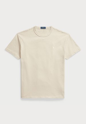 Beige kokvilnas T-krekls ar apaļu kaklu, īsām piedurknēm un mazu logo uz krūšu. Gluda tekstūra, ikdienišķa piegriezuma un minimāls dizains.