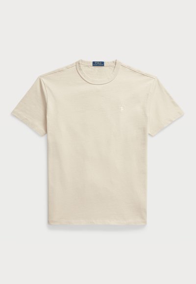 Beige bomullströja med rund hals, korta ärmar och en liten logotyp på bröstet. Lätt textur, avslappnad passform och minimalistisk design.