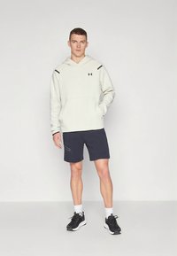 Light gray hoodie with dark accents, kangaroo pocket, paired with dark shorts featuring side details, and black athletic shoes.